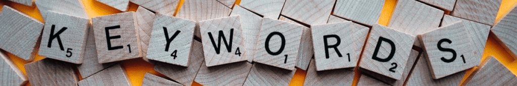 Lettres de Scrabble formant le mot "KEYWORDS" sur un fond jaune et gris.